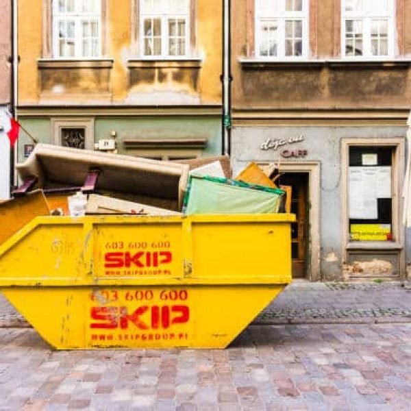Poznan, Poland - November 12, 2018: Full metal Skip container standing on a road in front of a damaged Deja Vu cafe in the city center.